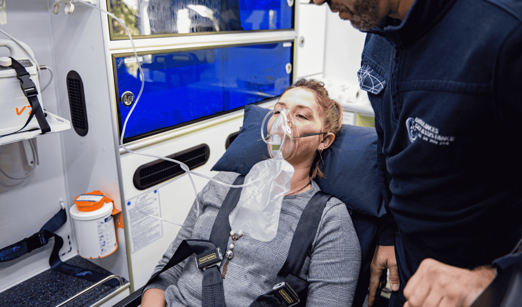 Ambulancier Dax Assistance prenant en charge une patiente sous masque à oxygène en position semi-assise, transport médicalisé vers Dax, Bayonne ou Mont-de-Marsan