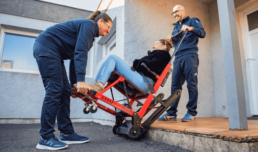 Deux ambulanciers Dax Assistance descendant une patiente en chaise portoir électrique depuis son domicile, pour un transport VSL vers Dax, Bayonne ou Mont-de-Marsan